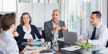 Business meeting Multiethnic group of business people sitting in annual meeting in conference room. Mature leader with businessmen and businesswomen discussing. Busy partners working together in modern office.